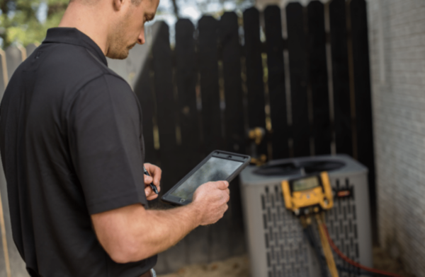 hvac technician looking at ipad while an outdoor hvac unit is having its pressure read in the background