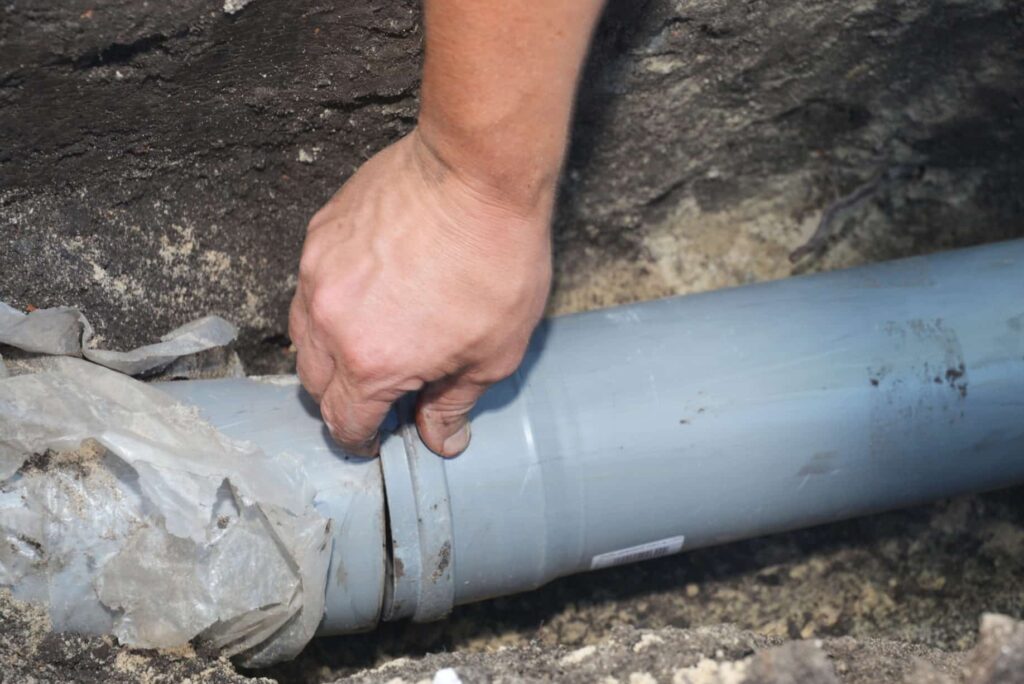 Contractor installing house sewer pipe in the ground trench